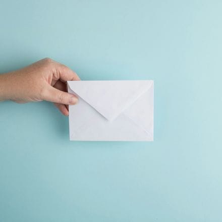 A hand holding up a sealed white envelope