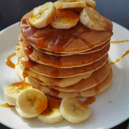 A stack of pancakes with sliced banana and syrup