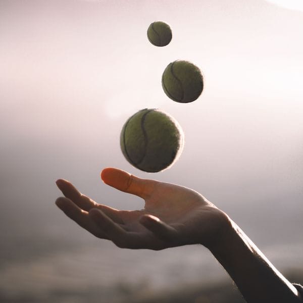 An open hand under three tennis balls tossed into the air